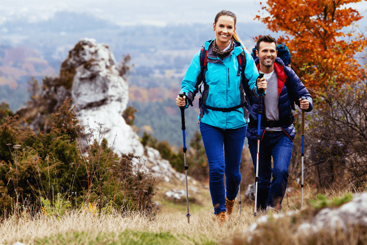 A couple use poles as they ascend a slope while trail running.