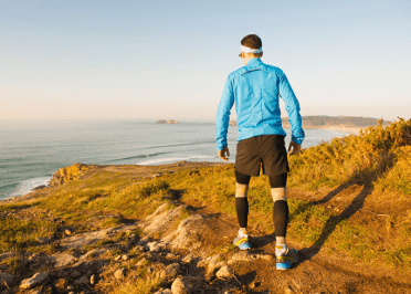 A male runner out on a running trail in the countryside builds up his pace slowly.