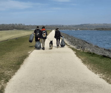 Three members of the Carsington Water litter-picking team walk along the long flat path beside the reservoir, carrying full bags of litter.