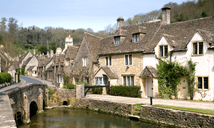 Honey-stone buildings sit beside an arched bridge over a low river in Castle Combe.