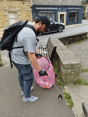 A member of the litter-picking team leans over to pick up a cigarette butt and bin it.