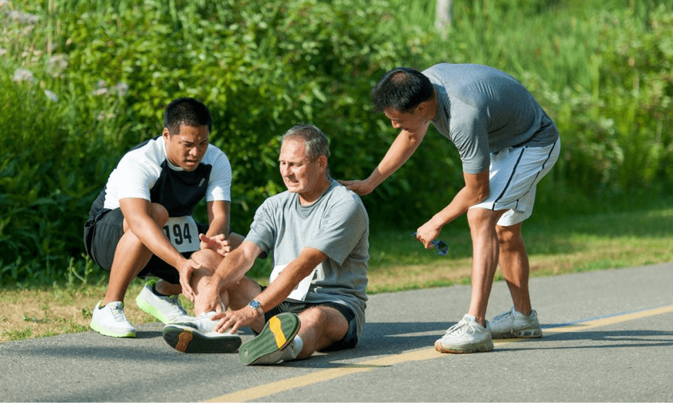 Two runners pause to assist a third injured runner partway through a race.