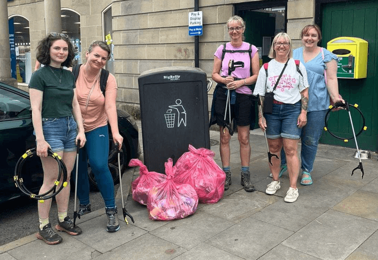 Five members of Contours' litter-picking crew pose beside a bin in Bakewell with their full bags of rubbish.