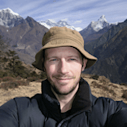Damian Hall, ultrarunner and writer of the Pennine Way guidebook, poses in front of mountains in an excellent hat.