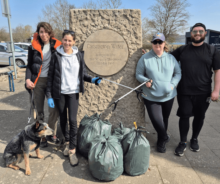 The litter-picking team from Contours stand in front of a plaque mounted on a large stone at Carsington Water, their full bin liners and litter-picking tools in hand.