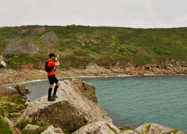 A trail runner stops to look out over the sea while running the South West Coast Path.