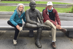 Two hikers sit on either side of a statue seated on a bench on their Contours Holiday.