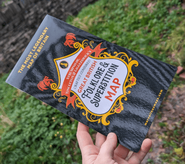 The Folklore map, with a shiny black cover, held outside in a grassy field.