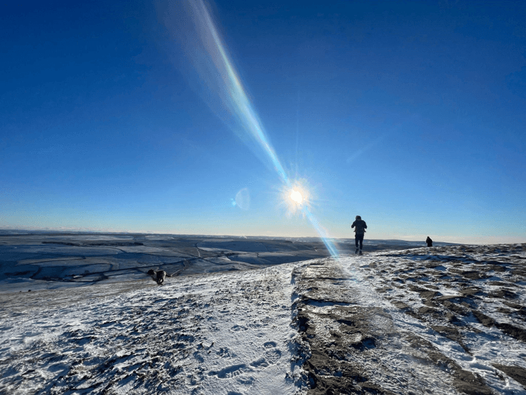 On a bright day, walkers and a dog explore Mam Tor on foot.