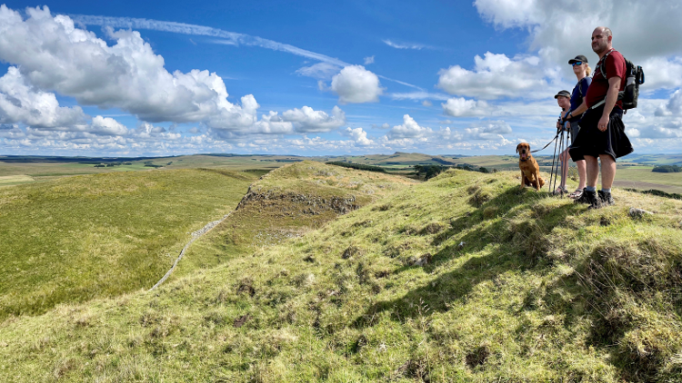 A group of walkers stand on a grassy peak in Northumberland.