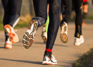 Three people run on tarmac. Hard surfaces like these are common causes of running injuries.