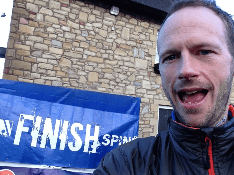 Damian Hall grins beneath the finish line banner at the end of the Spine Race.