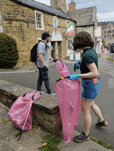 Two members of Contours Holidays' Eco Team use litter-pickers to collect rubbish from the centre of Bakewell and deposit it in red bags.