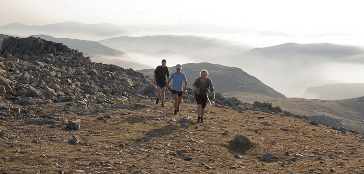 Clambering across rough ground toward Scafell Pike, a group of three adventurers could equally be walkers or runners.