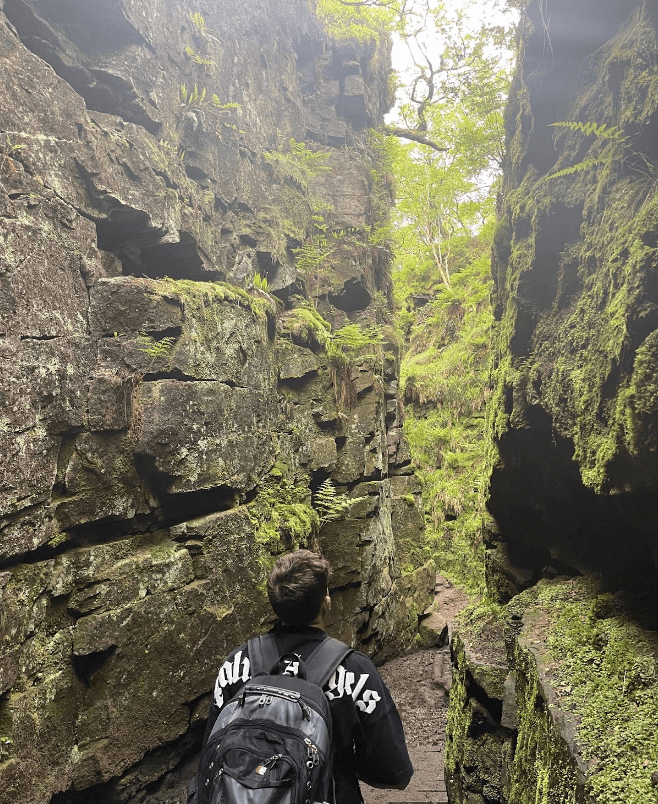 A walker wanders through the steep-sided stone gorge of Lud's Church.